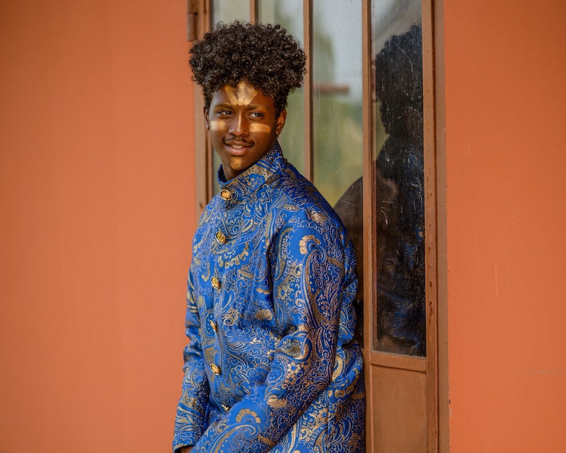 Person wearing a blue patterned coat standing against an orange wall.